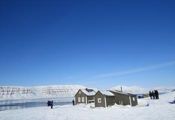 Fangstmanshytta i Fredheim ligger godt plassert i det snødekte terrenget. I bakgrunnen kan man se en fjord og en fjellformasjon.