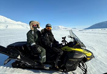 To personer sitter på en snøscooter i vinterlandskapet.