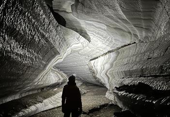 Person standing inside an ice cave with a head lamp
