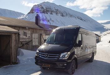 A minibus parked in front of a building with snow-covered mountains in the background