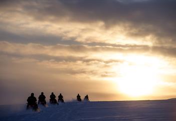Snowmobile tour group driving towards the sun
