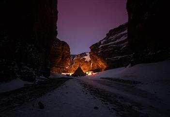 A tent is set up in a narrow valley. The sky is purple.