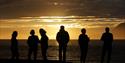 Persons in silhouette against the sun looking out over a fjord