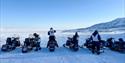 Gruppe mennesker med snøscootere på en åpen snødekt slette