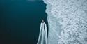 A boat cuts through sea ice viewed from above.