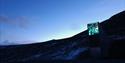 The entrance to Svalbard Global Seed Vault i dark lightly snowy surroundings with a blue and clear evening sky in the background