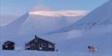 Villmarkshytte med snødekte fjell i bakgrunnen