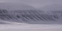 A guide and guests on snowmobiles in a landscape with mountains in the background