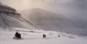 Guests on snowmobiles driving through a landscape with mountains in the background