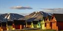 Colourful pointy houses in the foreground with a mountainous landscape and a slightly cloudy blue sky in th ebackground