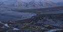 Longyearbyen and nearby snow-covered mountains seen from Platåfjellet with two persons hiking down a hill in the foreground