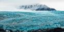 A glacier with a mountain in the background and a fjord in the foreground