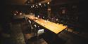 A room with a long table and chairs. The shelves are filled with winebottles from floor to celing.