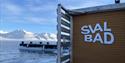SvalBad's logo on the exterior of the sauna with a fjord and snow-covered mountains in the background