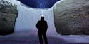 A person is standing in the dark with a headlamp, ligting up in the sky towards a frozen waterfall with snowy weather