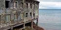 A old building on the edge of the water with the ocean in the horizon