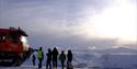 Persons standing next to a snowcat looking down towards Longyearbyen in the background