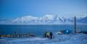 To gjester og en guide på sykler i Longyearbyen med fjell og en fjord i bakgrunnen