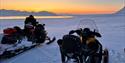 En guide på snøscooter ved iskanten i solnedgangen.