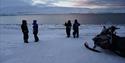 Guests and a snowmobile standing next to the shoreline