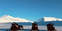 Tre parkerte snøscootere på snøen med klar blå himmel