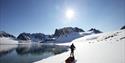 A person skiing and pulling a sled along a shoreline