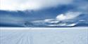 Snødekt dal omgitt av fjell, med snøscooterspor som leder innover landskapet.