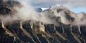 A mountain face with clouds of mist swirling in between mountain ridges along the face