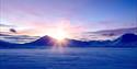 Frozen tundra in the foreground, with a sunset behind the mountains in the background.