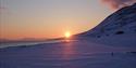 The midnight sun partially hidden by a mountain ridge