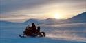Snøscooter som kjører med sol og fjell i bakgrunnen