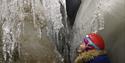One person with a headlamp and helmet studying the ice inside of an ice cave
