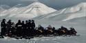 A group of people are standing in the winter landscape around snowmobiles