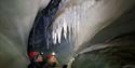 two people with headlamps and helmets admiring the formations on the ceiling of the ice cave.