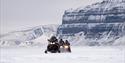 Two snowmobiles in front of a steep mountainside.