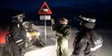 tre mennesker står ved isbjørnskiltet med ATV ved siden av