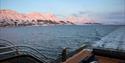 Person on the back deck on a boat, enjoying the view of the sea and mountains in the background