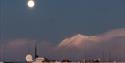 Isfjord Radio in a snowy landscape with mist over the fjord in the background and the moon shining above.