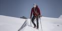 A person with glacier safety equipment hiking on a glacier