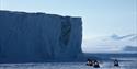 A tour group on snowmobiles with an ice wall in the background