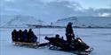 A guide driving a snowmobile with guests on the sled being pulled behind