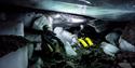 Persons lying inside a dark icecave, lighting up the ice covered cave with a headlamp.