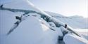 Two people walk up a mountain of ice in a snowy landscape.