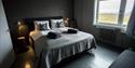 Et hotellrom i grå farger med en dobbeltseng hvor det ligger puter og håndklær på senga.