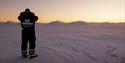 En guide fra Snowfox Travel står på snødekket vidde og ser utover landskapet i solnedgangen.