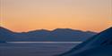 Snødekte fjell og havis badet i oransje solnedgangsfarger.