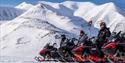 flere personer på snøscootere i fjellandskap