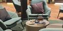 A small table with a coffee pot, a book and a coffee cup in the middle of a group of chairs in a hotel lobby