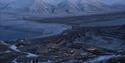 Longyearbyen og snødekte fjell i nærområdet sett fra Platåfjellet med to personer som går ned en fjellside i forgrunnen