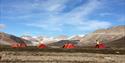 Four tents on the tundra with mountains and glaciers in the background.